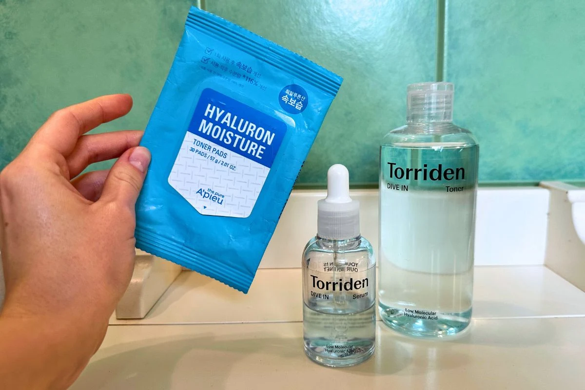 Zestaw kosmetyków pielęgnacyjnych do twarzy obejmujący płyn do tonizacji, serum z pipetą oraz opakowanie płatków tonizujących, umieszczone na tle zielonych płytek łazienkowych.