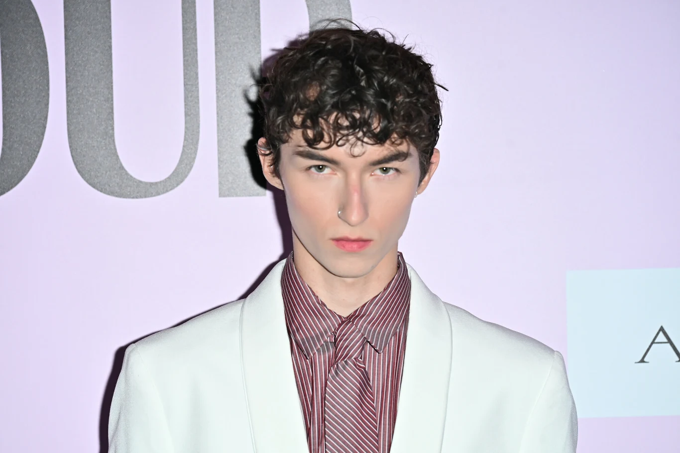 Marcin Maciejczak wyznał, że nie chciał brać udziału w Eurowizji Junior Młody mężczyzna o jasnej karnacji i ciemnych, kręconych włosach ubrany w biały garnitur i pasiastą koszulę w odcieniach czerwieni, pozujący na tle ściany z jasnym napisem.