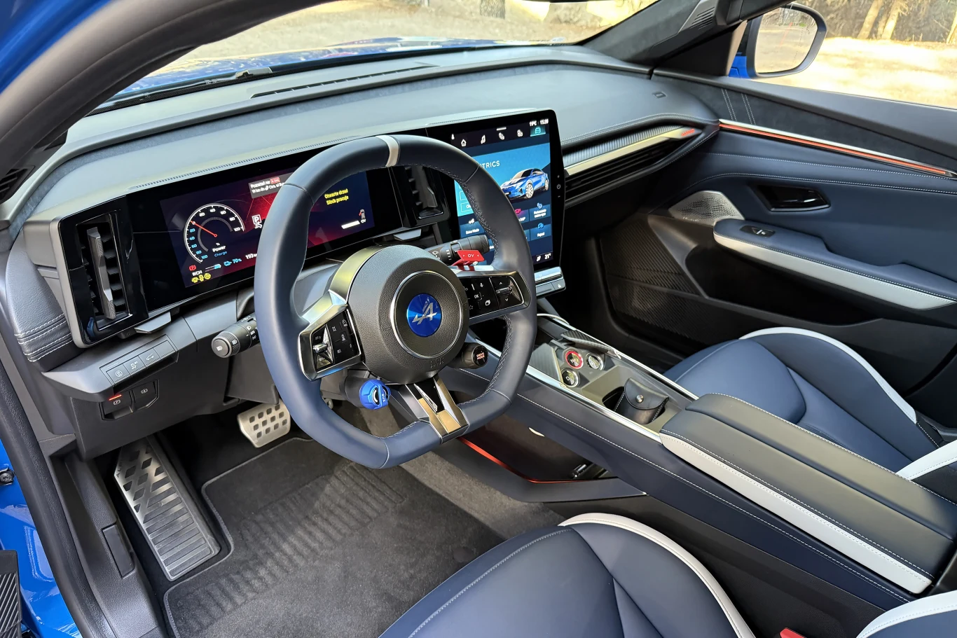 Wnętrze nowoczesnego samochodu z cyfrowym kokpitem, dużym ekranem centralnym i sportową kierownicą ozdobioną charakterystycznym niebieskim logo Subaru. Fotele pokryte skórzaną tapicerką, w kabinie dominuje stylowe wykończenie i zaawansowane technologie.