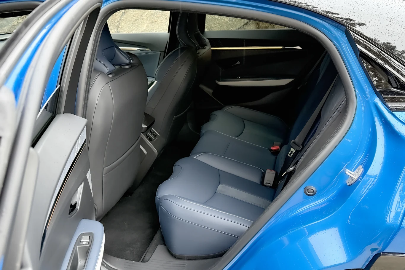 Otwarta tylna część niebieskiego samochodu z wyraźnie widocznymi tylnymi siedzeniami i elegancką tapicerką, czyste wnętrze oraz dobrze oświetlone siedzenia pasażerów.