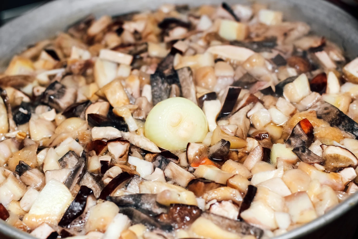 Pokrojone grzyby, cebula oraz inne warzywa gotujące się w garnku, tworząc potrawę o bogatej strukturze i intensywnym aromacie.