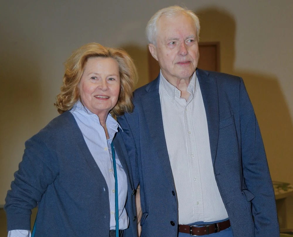 Barbara Bursztynowicz ujawniła prawdę o relacji z mężem Starsza kobieta i starszy mężczyzna stoją razem, uśmiechają się, ubrani w eleganckie, casualowe ubrania w odcieniach niebieskiego i szarości. Tło jest neutralne i nie zwraca na siebie uwagi.