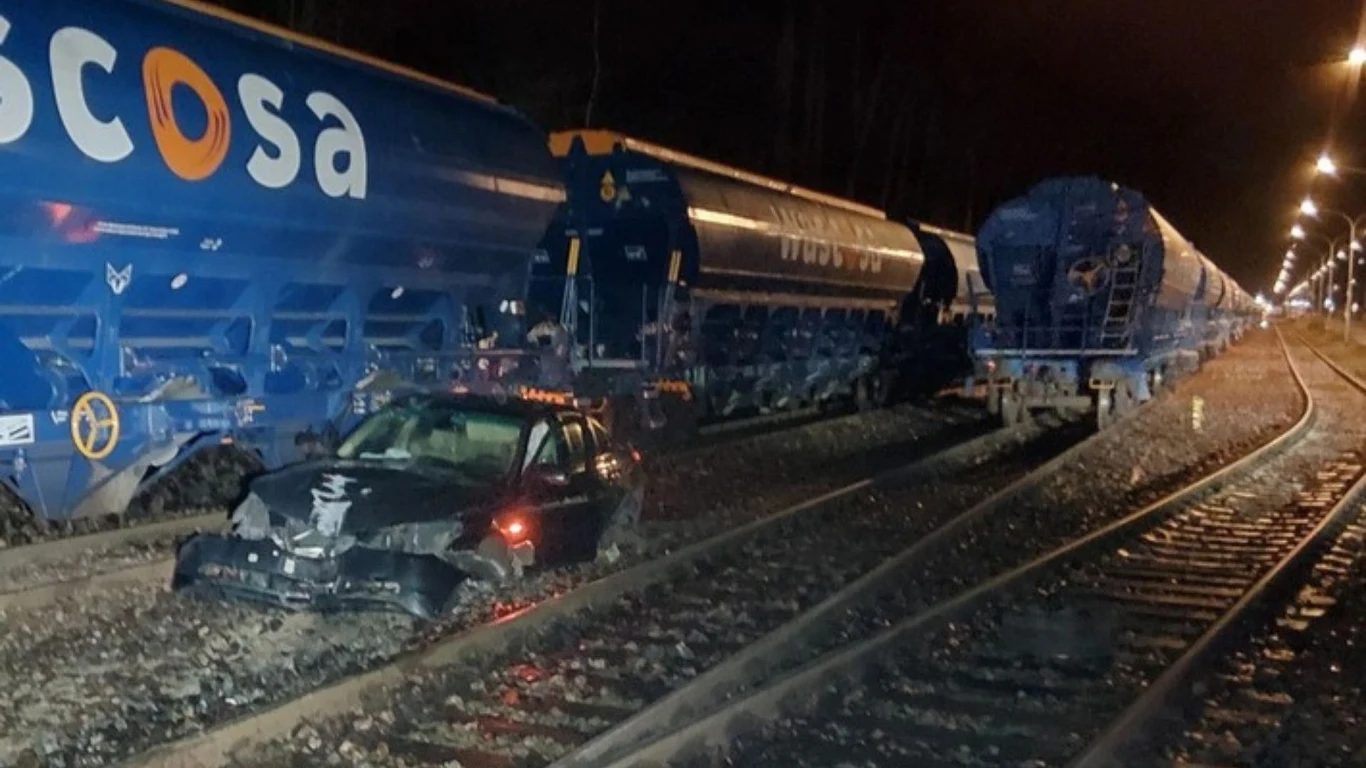 Polak rozbił swoje bmw, uszkadzając wagon i torowisko w Rostocku Uszkodzony czarny samochód osobowy znajduje się na torach kolejowych obok niebieskich wagonów towarowych, całość oświetlona lampami ulicznymi, akcja odbywa się nocą.