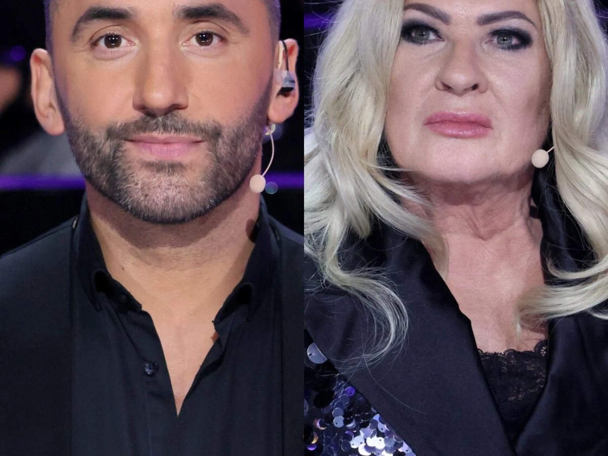 Dwie osoby, kobieta i mężczyzna, w formalnych ubraniach siedzą obok siebie w studio telewizyjnym, oboje mają zamocowane mikrofony nagłowne. Kobieta ma długie blond włosy, mężczyzna krótko przystrzyżoną brodę.