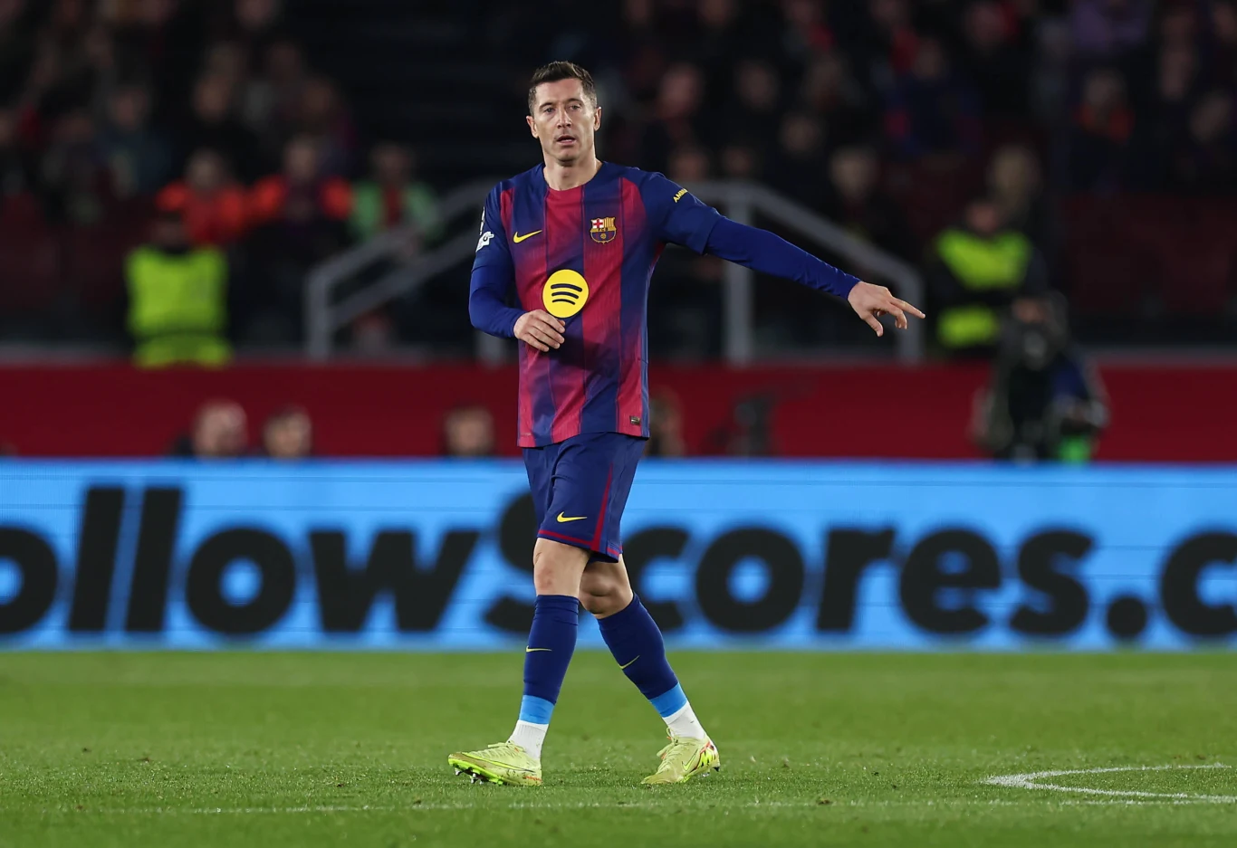 Piłkarz w stroju FC Barcelony stoi na murawie stadionu w trakcie meczu, w tle widać rozmytych kibiców oraz tablicę reklamową.