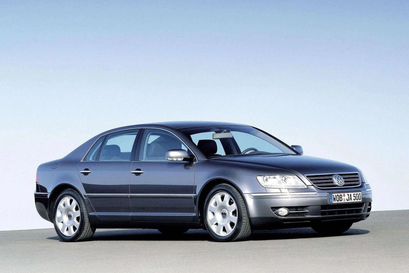 Volkswagen Phaeton Srebrny sedan marki Volkswagen Phaeton ustawiony na tle czystego, niebieskiego nieba, wyróżniający się nowoczesnym wyglądem, dużymi reflektorami i aluminiowymi felgami.