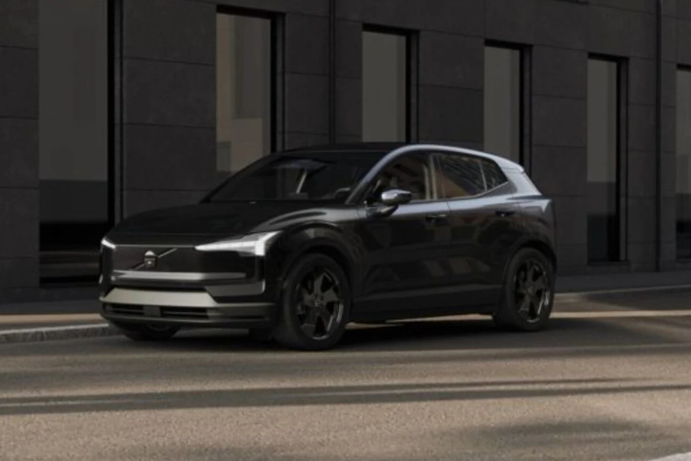 Volvo EX30 Black Edition, z niewielkimi wyjątkami, jest z zewnątrz całe czarne Czarny nowoczesny SUV marki Volvo stoi zaparkowany przy ulicy, w tle znajduje się fasada budynku z dużymi oknami.