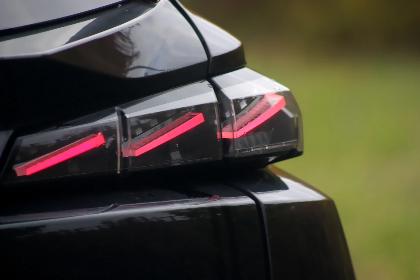 Tylna lampa LED nowoczesnego samochodu w kolorze czarnym, z jasnoczerwonymi światłami włączonymi, fragment błyszczącej karoserii i rozmyte zielone tło.
