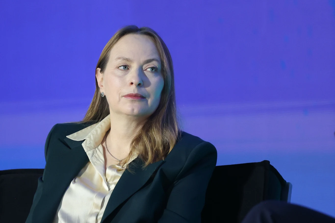 Ministerstwo funduszy, którym kieruje Katarzyna Pełczyńska-Nałęcz, poinformowało, że ECOFIN wydała zgodę na finalną rewizję polskiego KPO Kobieta w średnim wieku w eleganckim garniturze i jasnej koszuli siedząca na czarnym fotelu na tle niebieskiego światła, z poważnym wyrazem twarzy i jasnymi włosami opadającymi na ramiona.