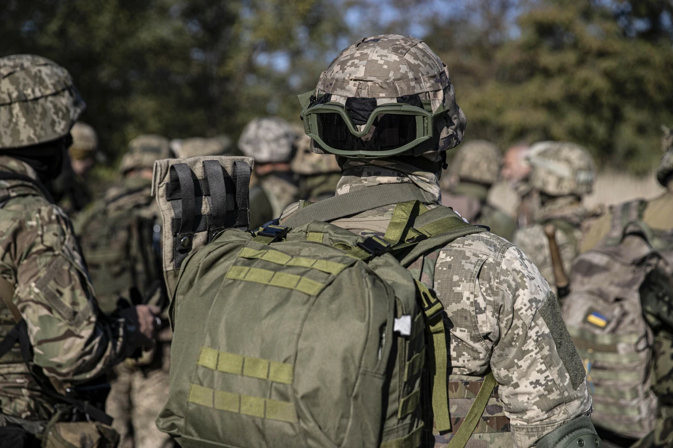 Ukraińscy żołnierze zamiast odbywać służbę wojskową, pracowali w warsztacie samochodowym Grupa żołnierzy ubranych w mundury wojskowe i wyposażonych w plecaki oraz sprzęt bojowy zgromadzona na otwartym terenie, w tle drzewa i rozmyte sylwetki kolejnych wojskowych.