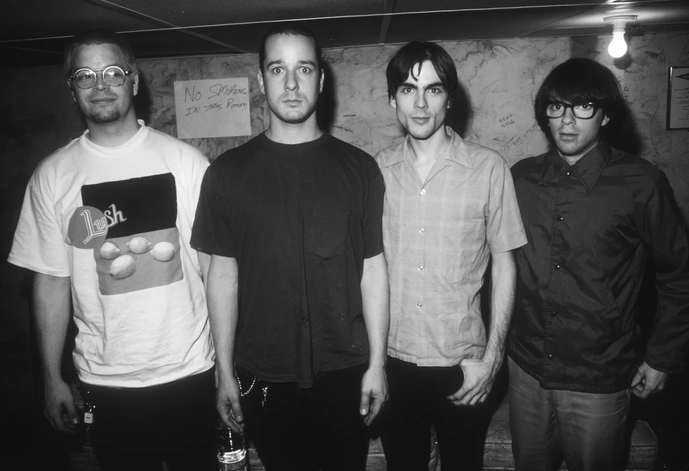 Weezer w 1994 r. - od lewej: Patrick Wilson, Matt Sharp, Brian Bell i Rivers Cuomo Czterech mężczyzn stoi obok siebie na tle ściany z widocznymi odręcznymi napisami. Wszyscy ubrani są w codzienne, niezobowiązujące ubrania, a oświetlenie jest stonowane, sprawiając wrażenie zdjęcia wykonanego w pomieszczeniu zamkniętym.