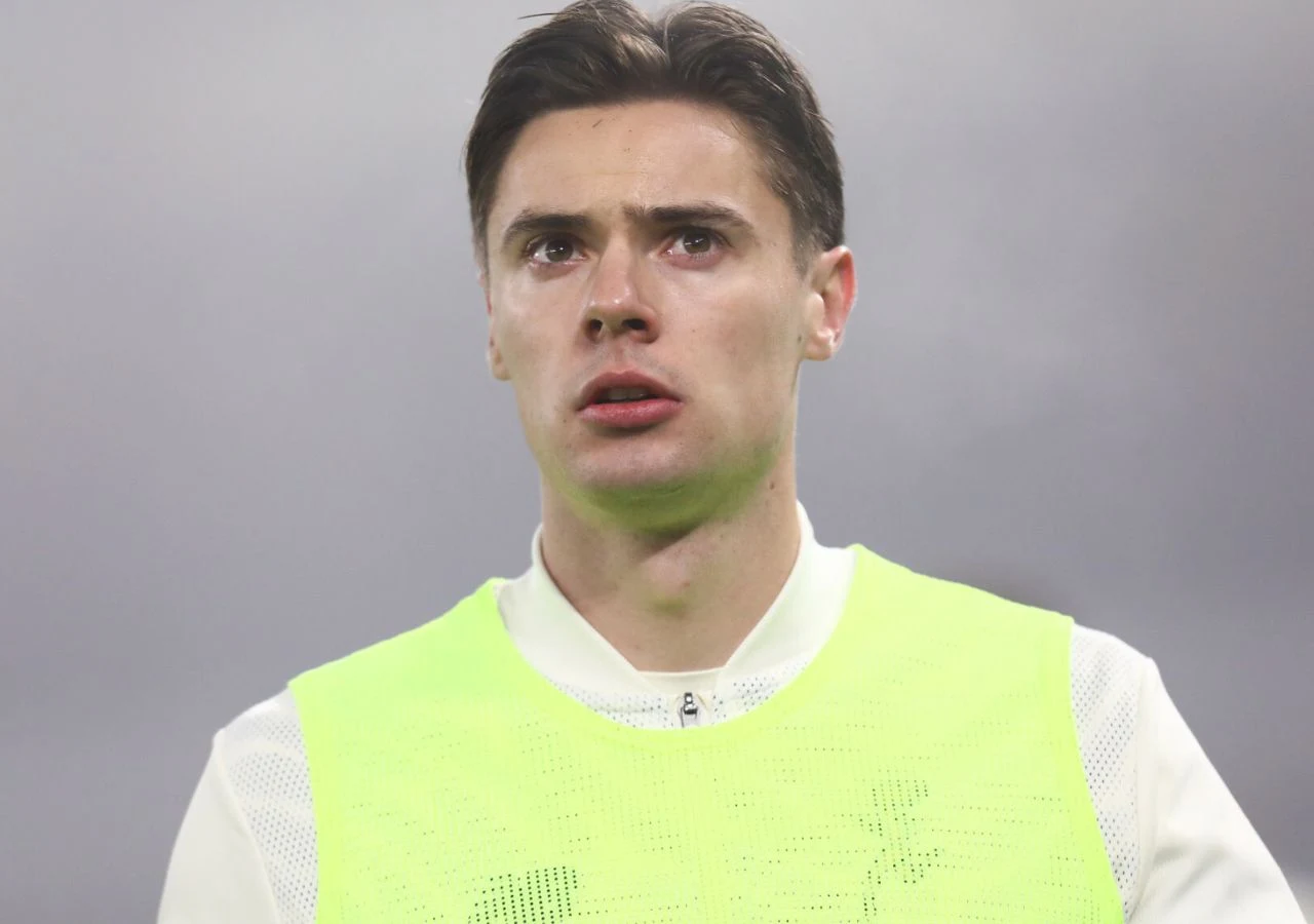 Nicola Zalewski Młody mężczyzna o ciemnych włosach patrzy przed siebie z poważnym wyrazem twarzy, ubrany w jasny strój sportowy i fluorescencyjną kamizelkę, na tle szarego, rozmytego nieba.