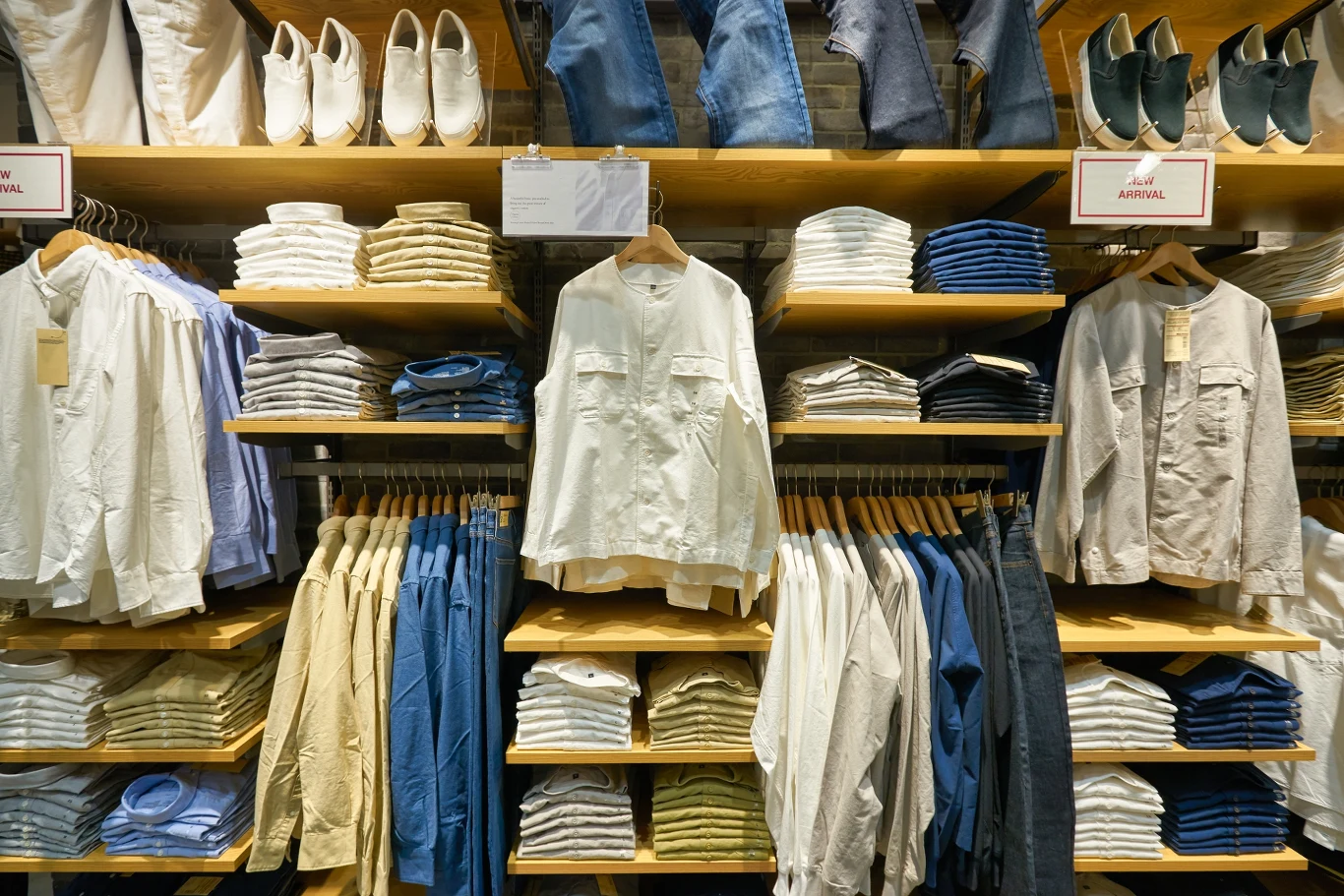 W ubraniach jest więcej toksyn niż nam się zdaje Równo poukładane koszule i spodnie na półkach oraz zawieszone na wieszakach, w tle widoczne półki z dodatkowymi ubraniami i butami. Wyeksponowana biała koszula wisząca na wieszaku pośrodku kompozycji.