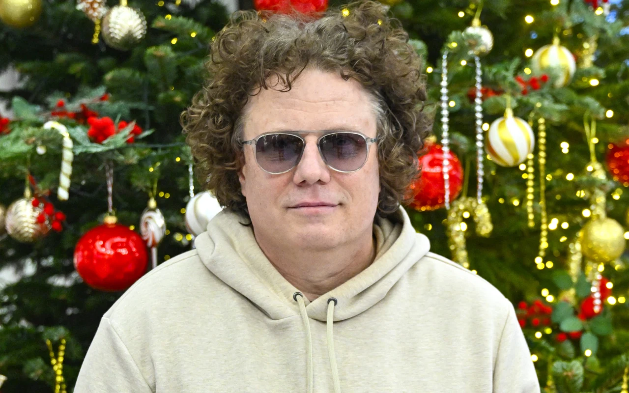 Sidney Polak w jasnej bluzie, okularach, na tle choinki