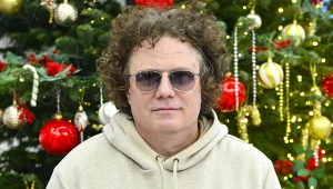 Sidney Polak w jasnej bluzie, okularach, na tle choinki