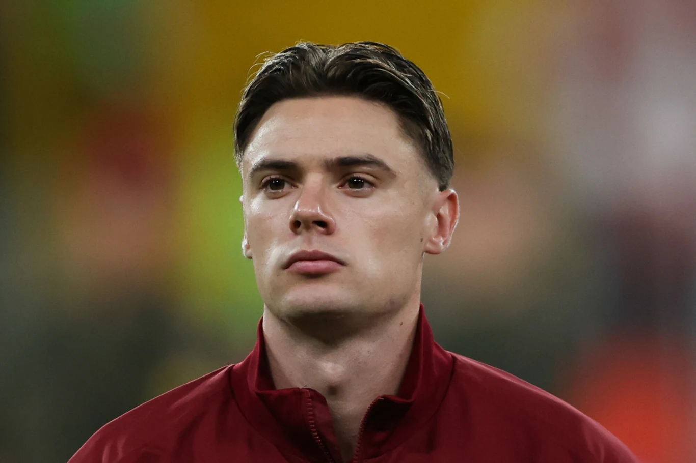 Nicola Zalewski Młody mężczyzna w bordowej kurtce sportowej na tle żółto-zielonym z niewyraźnym tłem, wyraz twarzy poważny i skupiony, włosy ułożone do tyłu.