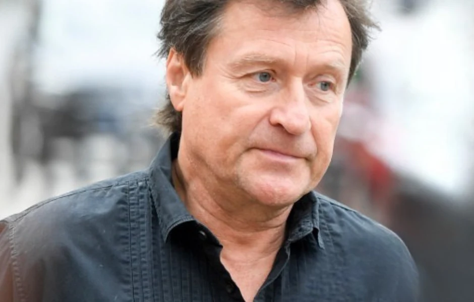 Jacek Kawalec Mężczyzna w średnim wieku ubrany w ciemną koszulę, z lekko rozczochranymi włosami, patrzący lekko w bok. Tło rozmyte, bez wyraźnych szczegółów.