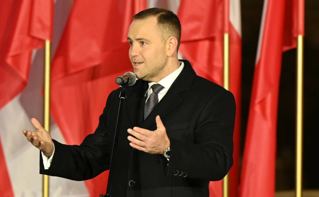 Prezydent Karol Nawrocki przemówił podczas uroczystego zapalenia "Światła Wolności" w 44. rocznicę wprowadzenia w Polsce stanu wojennego. Mężczyzna w ciemnym płaszczu i krawacie przemawia do mikrofonu, gestykulując dłońmi, w tle liczne biało-czerwone flagi.