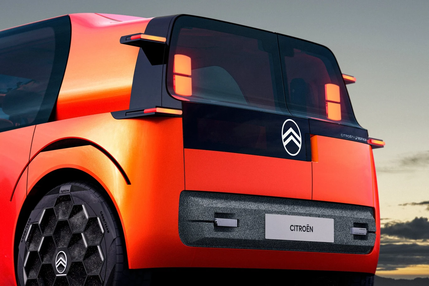 Klapa bagażnika Citroena ELO jest asymetryczna i przeszklona Nowoczesny, pomarańczowy samochód Citroën z kanciastymi kształtami, dużymi szybami oraz designerskimi, sześciokątnymi felgami na tle zachmurzonego nieba.