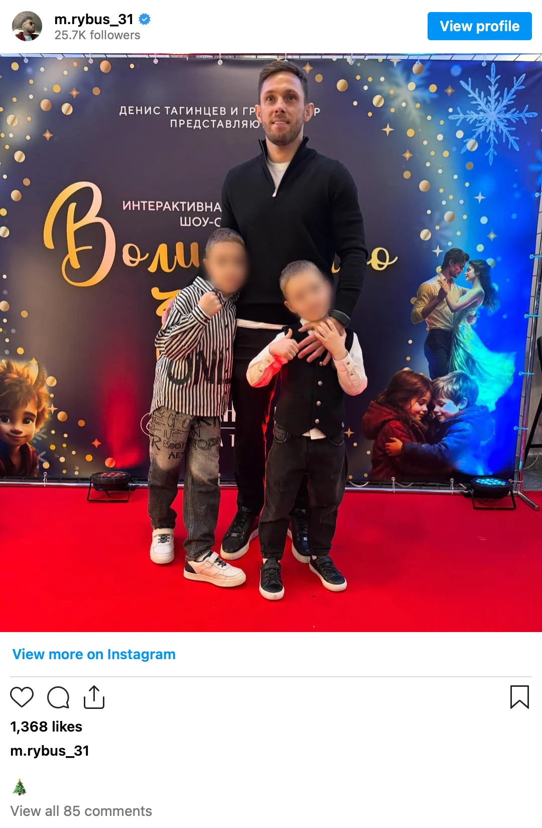 Mężczyzna pozuje z dwójką dzieci na tle dekoracyjnej ścianki z napisem i gwiazdkowym motywem, całość ustawiona na czerwonym dywanie.