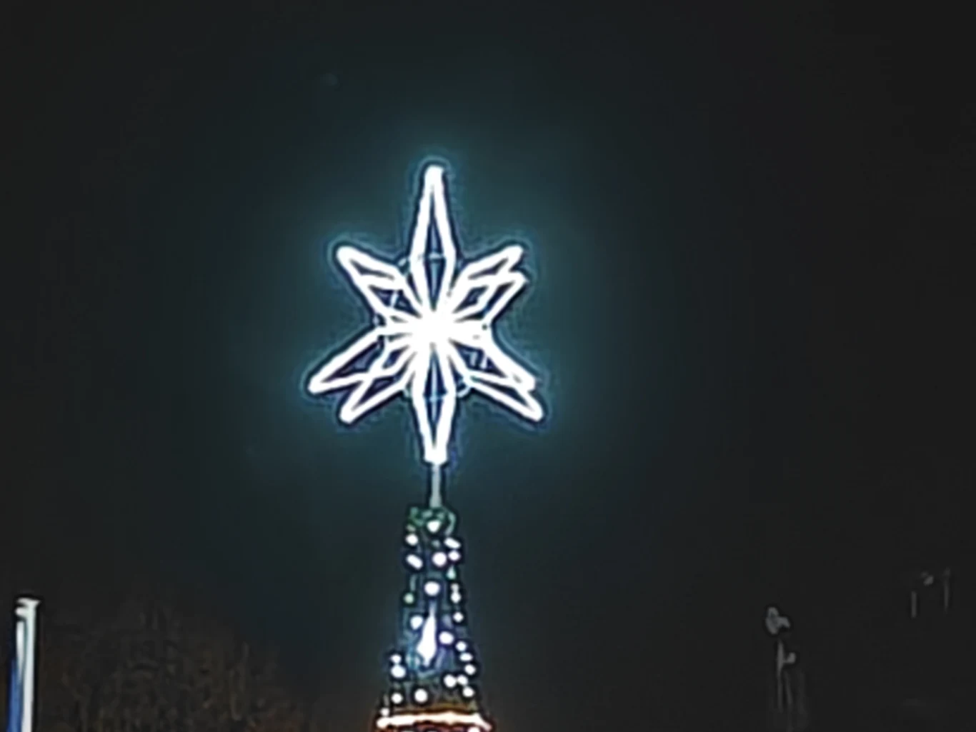 Oświetlona ledowa gwiazda na szczycie świątecznego drzewka, umieszczona na tle ciemnego nocnego nieba.