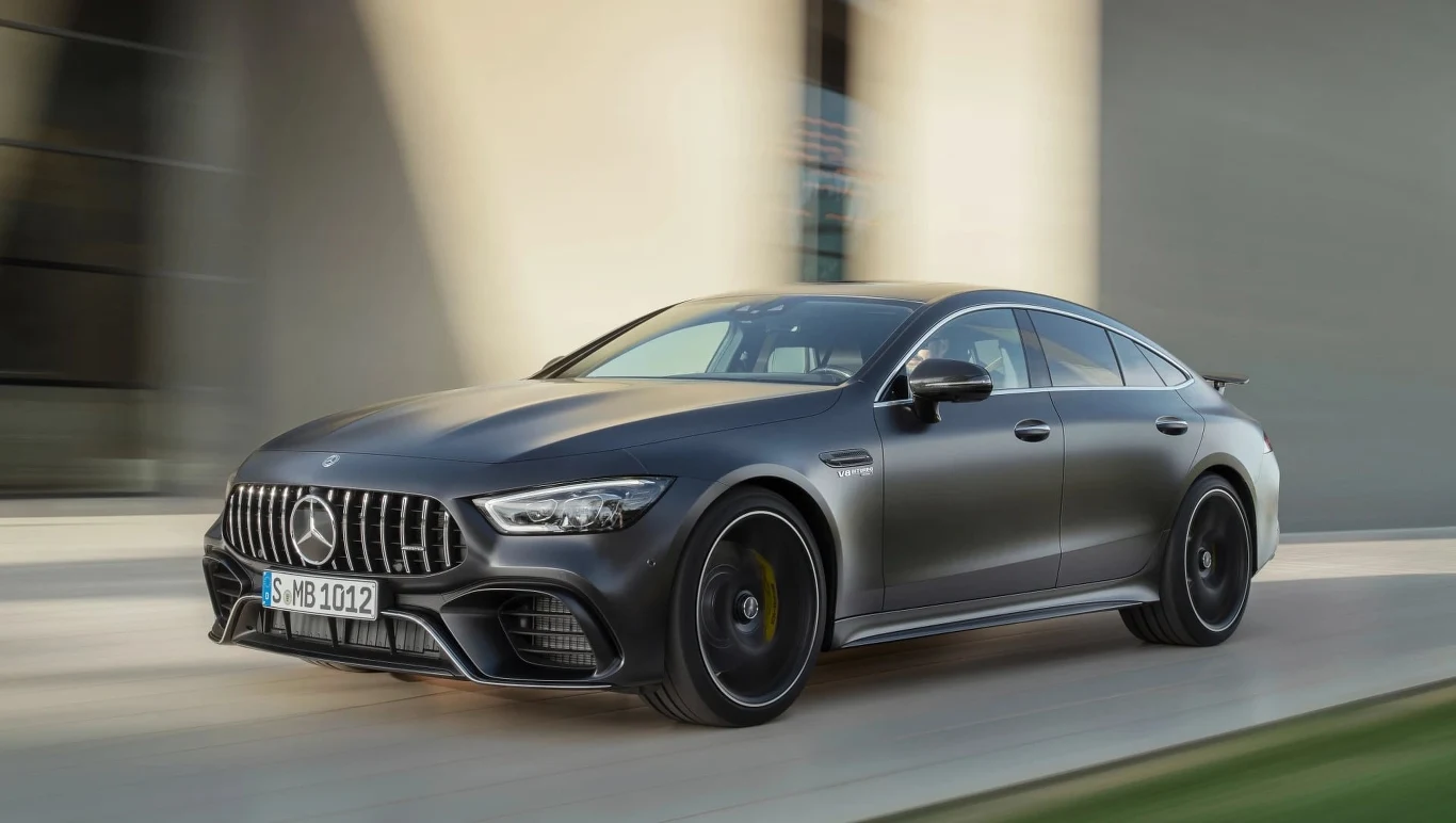 Sportowy samochód Mercedes-AMG GT w kolorze matowej czerni, jadący dynamicznie po miejskiej drodze, widoczne charakterystyczne logo AMG na grillu, aerodynamiczna sylwetka oraz aluminiowe felgi.