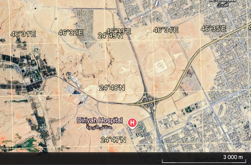 Satelitarny widok obszaru miejskiego i pustynnego z oznaczonym szpitalem Diriyah Hospital, siecią dróg oraz współrzędnymi geograficznymi; widoczne rzadkie zabudowania, gęsta infrastruktura drogowa oraz rozległe tereny pustynne.