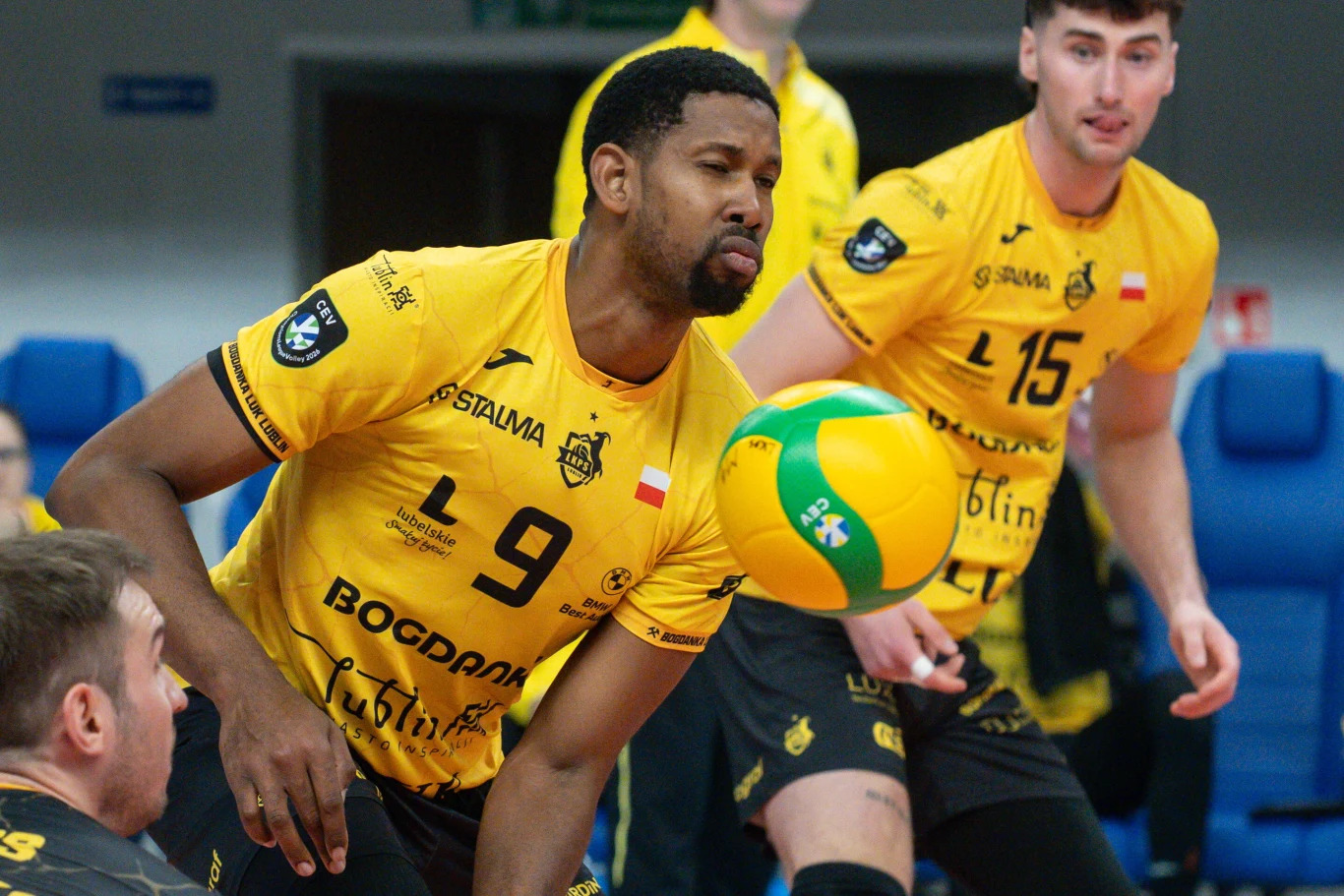 Dwóch siatkarzy w żółtych koszulkach skupionych podczas gry, jeden z nich odbija piłkę, a drugi obserwuje przebieg akcji.