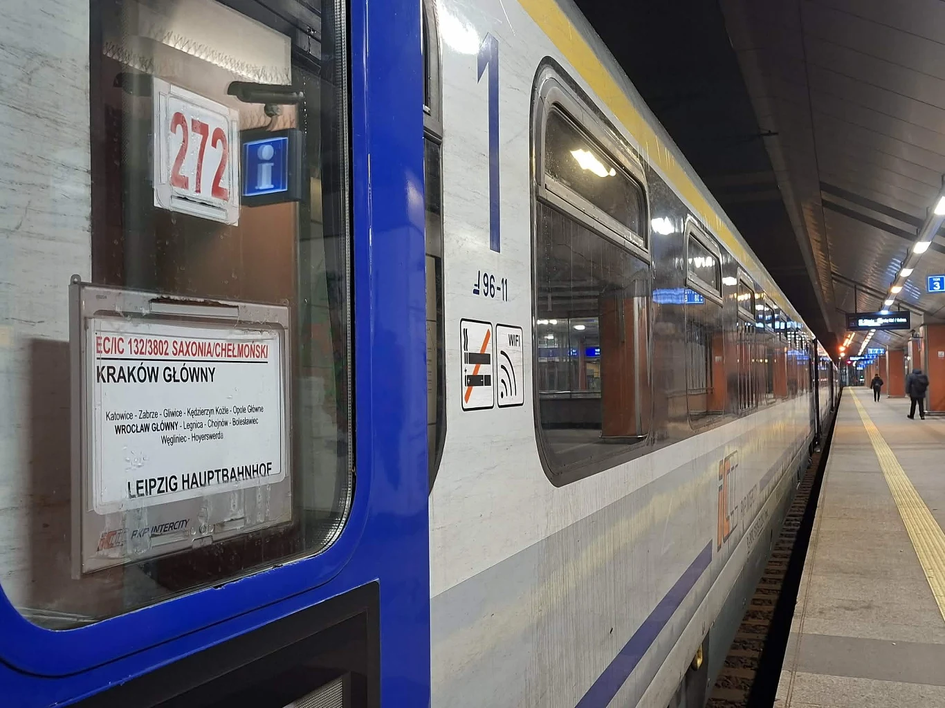 Debiutancki kurs EC "Saxonia" do Lipska Wagon kolejowy międzynarodowego pociągu nocnego zatrzymany przy peronie na dużej stacji, na szybie widoczna tablica kierunkowa informująca o trasie z Krakowa Głównego do Lipska, peron oświetlony z widocznymi podróżnymi.