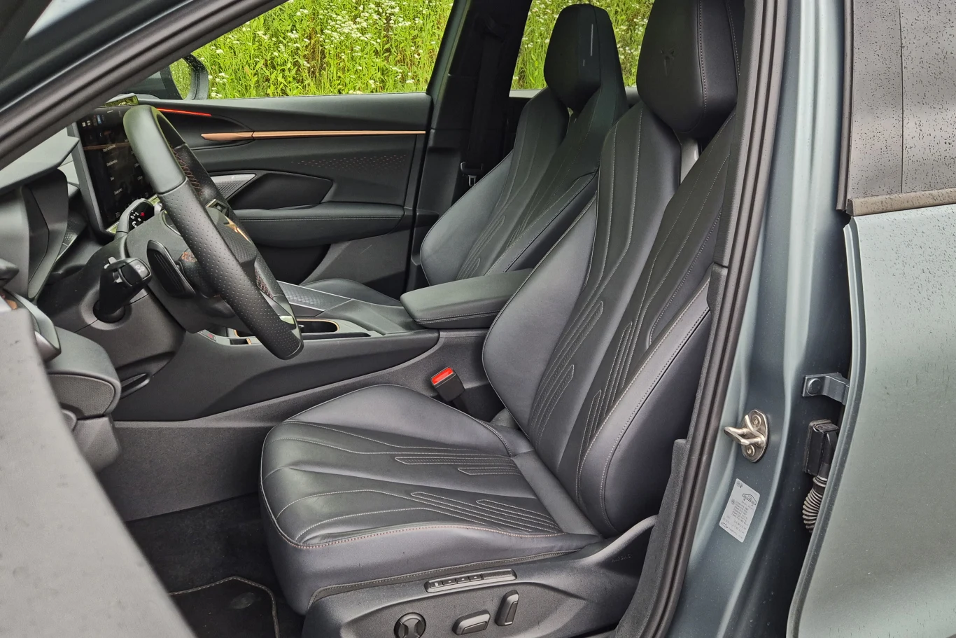 Wnętrze nowoczesnego samochodu z widocznymi dwoma siedzeniami pokrytymi czarną skórą, deską rozdzielczą z kierownicą oraz panelami drzwiowymi z eleganckimi detalami. Jasne, czyste linie i dobre wykończenie podkreślają komfort oraz estetykę samochodu.