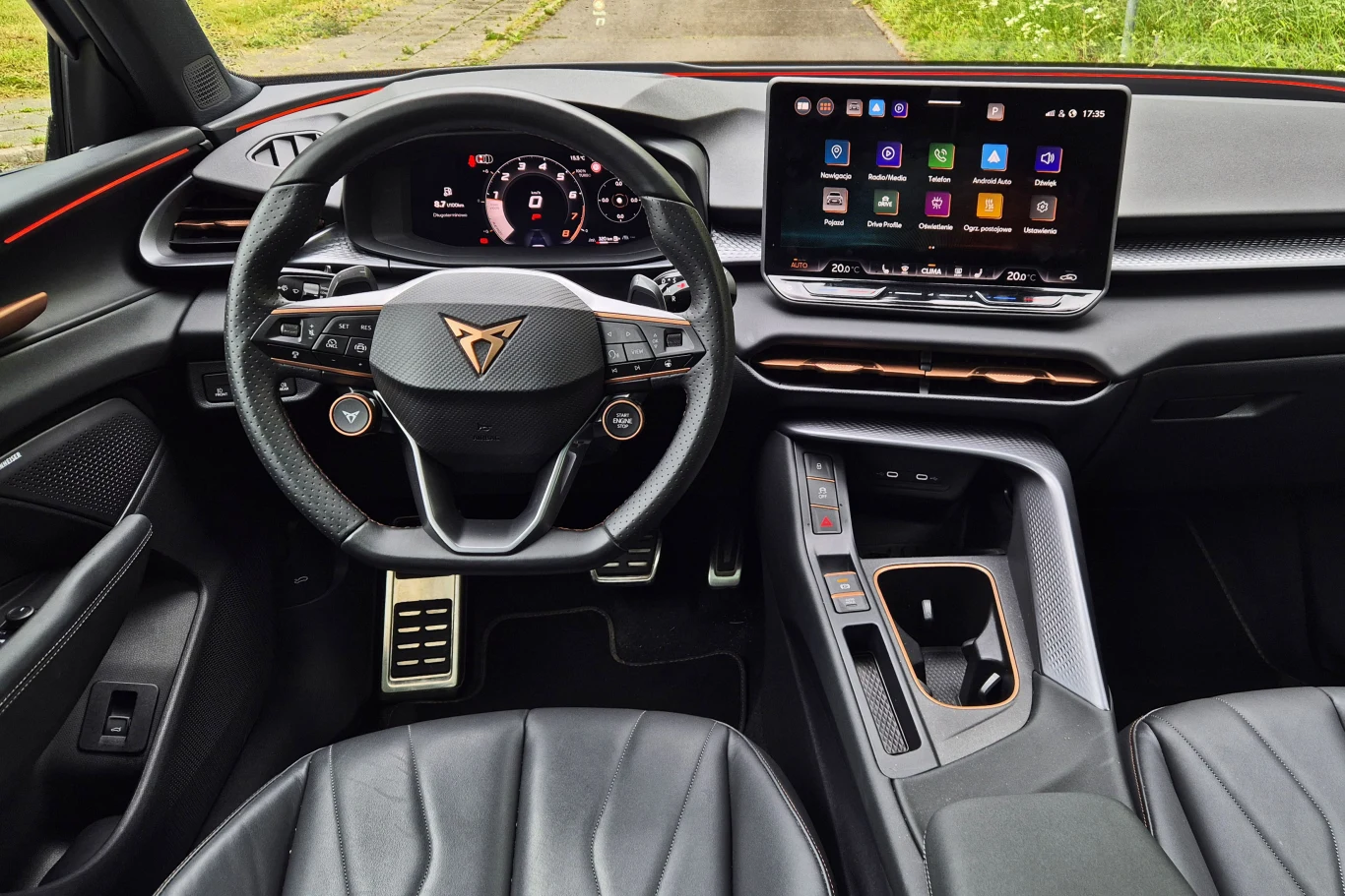 Wnętrze nowoczesnego samochodu z cyfrowym kokpitem, wielofunkcyjną kierownicą oraz centralnym ekranem dotykowym wyświetlającym system multimedialny, skórzane fotele i sportowe wykończenia.