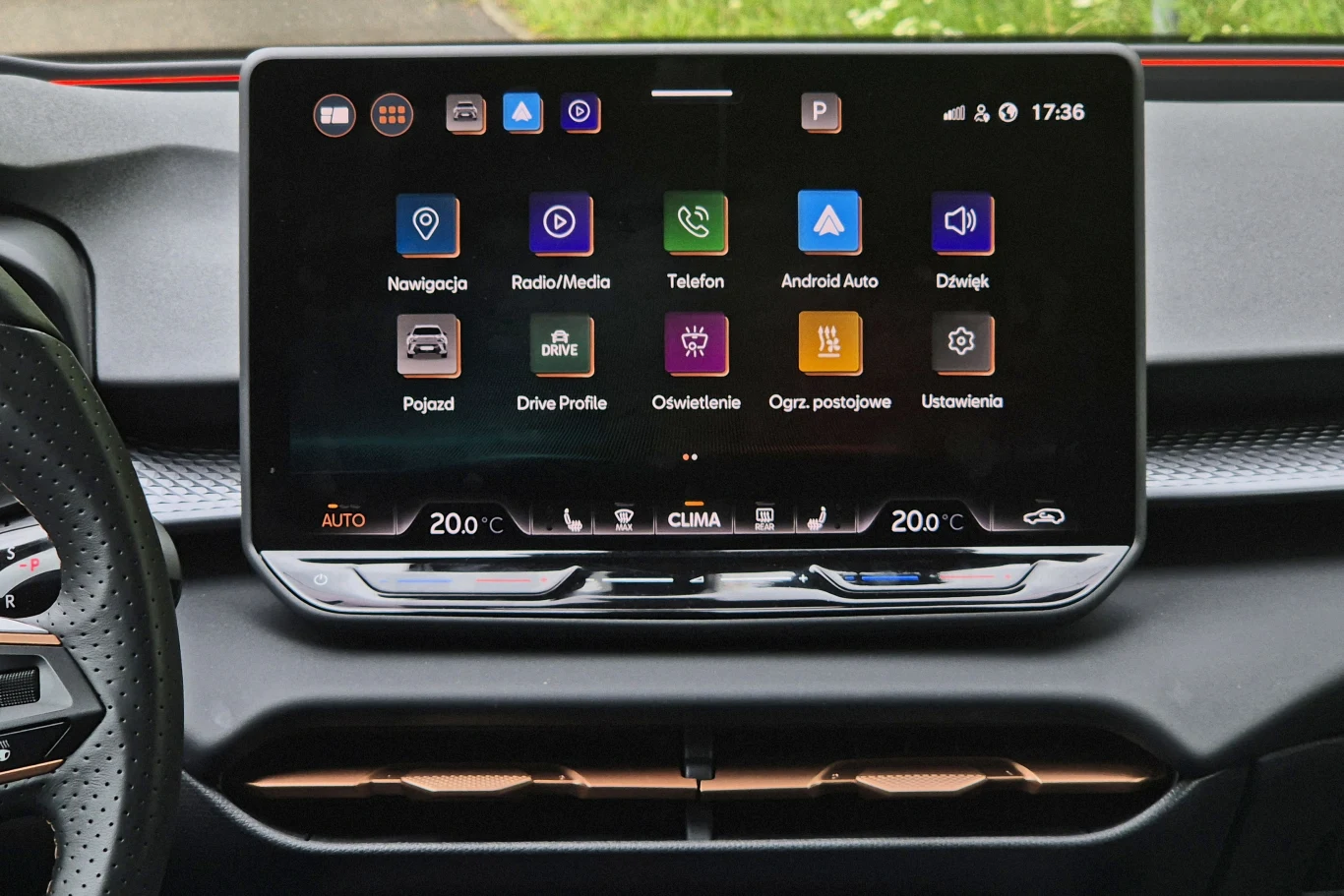 Dotykowy ekran systemu multimedialnego w samochodzie z widocznymi ikonami nawigacji, radia, telefonu, ustawień oraz sterowaniem klimatyzacją, osadzony na desce rozdzielczej.