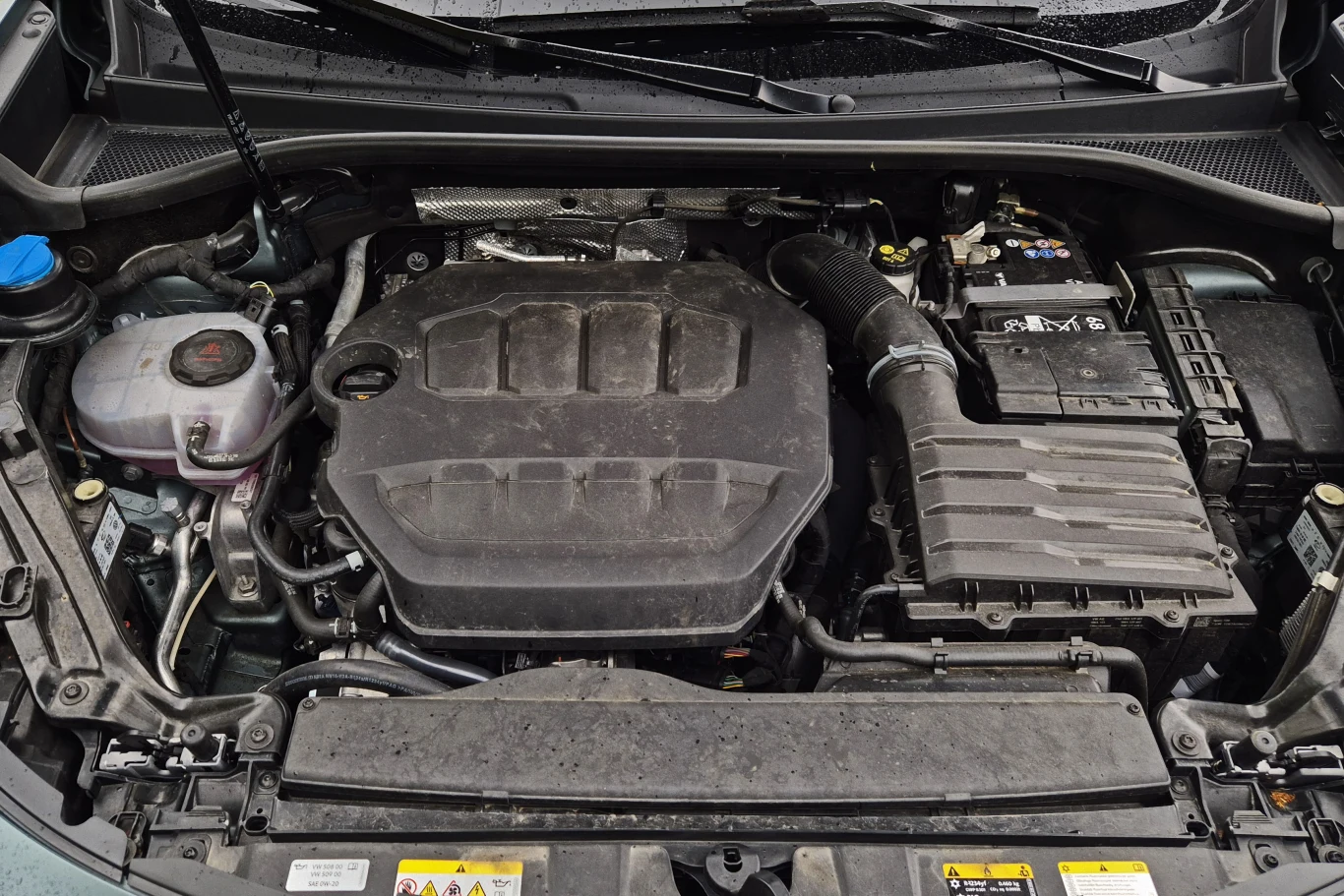 Komora silnika samochodu z widocznym silnikiem benzynowym, akumulatorem, zbiornikiem płynu chłodzącego oraz innymi elementami układu mechanicznego.