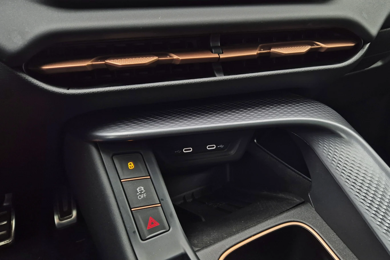 Konsola środkowa samochodu z widocznymi przyciskami blokady drzwi, wyłączania systemu ESP oraz światłami awaryjnymi, podwójnym portem USB-C oraz kratkami nawiewu.