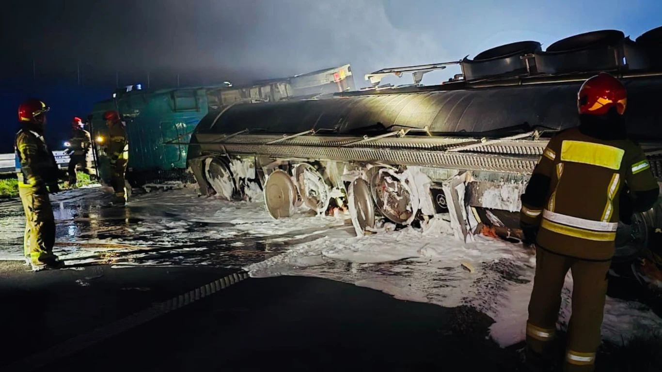 Wypadek w Podlaskiem. Przewrócona cysterna ze spirytusem Strażacy w specjalnych kombinezonach przebywają przy przewróconej cysternie, z której wydobywa się para, wokół widoczne są ślady piany gaśniczej, atmosfera nocna i akcja ratownicza w toku.