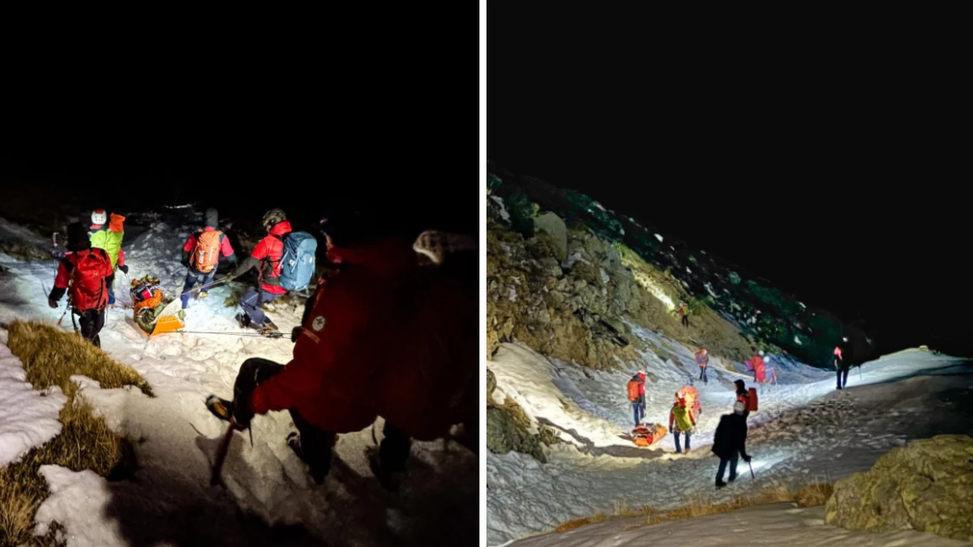 Grupa ratowników górskich w odblaskowych kurtkach prowadzi akcję ratunkową nocą na zaśnieżonym, stromym zboczu, używając latarek oraz noszy do transportu poszkodowanego, wokół strome skały i ciemność.