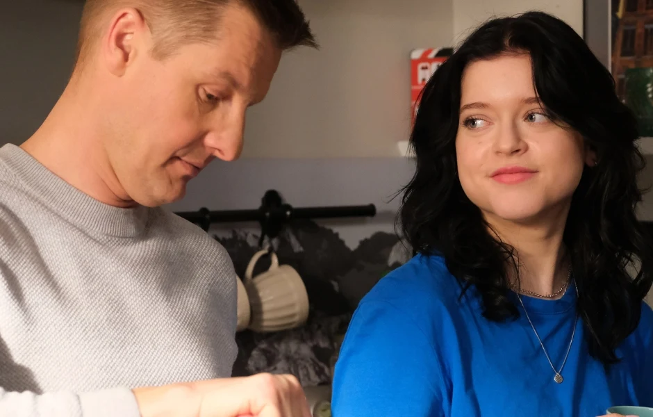 Gabriela Raczyńska grała Basię w "M jak miłość" Dwoje ludzi w kuchni, mężczyzna skupiony na czynności manualnej, kobieta z ciemnymi włosami patrzy na niego z lekkim uśmiechem. W tle kuchenne akcesoria i stonowane kolory.