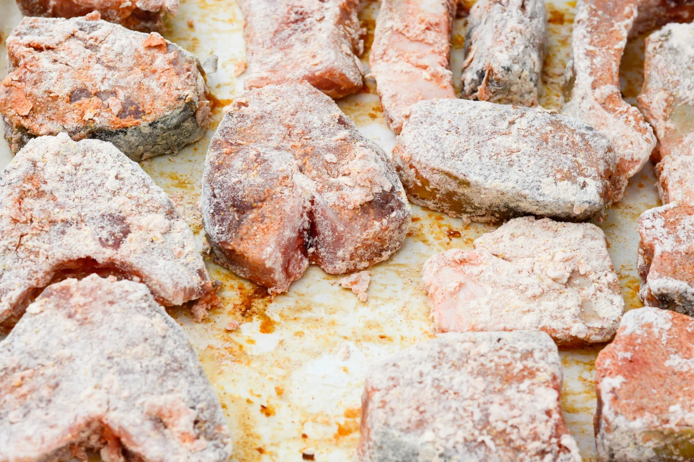 Surowe kawałki ryby obtoczone w mące, ułożone na blasze do pieczenia, lekko przypudrowane i gotowe do dalszej obróbki kulinarnej.