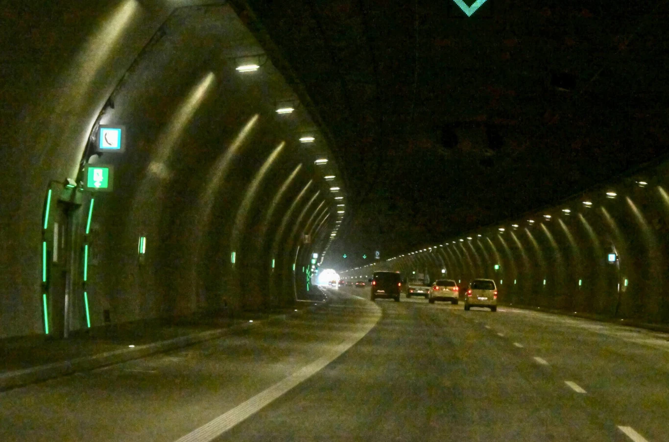Tunel na Zakopiance przeżywa oblężenie Wnętrze oświetlonego tunelu drogowego z kilkoma samochodami jadącymi w jednym kierunku, po bokach widoczne zielone oznaczenia wyjścia awaryjnego oraz ściany pokryte lampami.