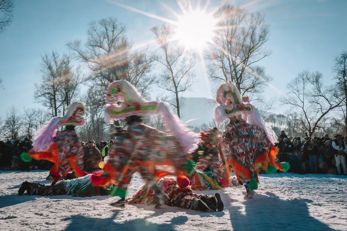 Dziady Noworoczne to jedyna taka tradycja w Polsce. Występuje tylko na Żywiecczyźnie Grupa osób ubranych w kolorowe, tradycyjne stroje uczestniczy w folklorystycznym widowisku na śniegu, wokół zgromadzona jest widownia, a w tle widoczne są nagie drzewa i słońce świecące nisko na niebie.