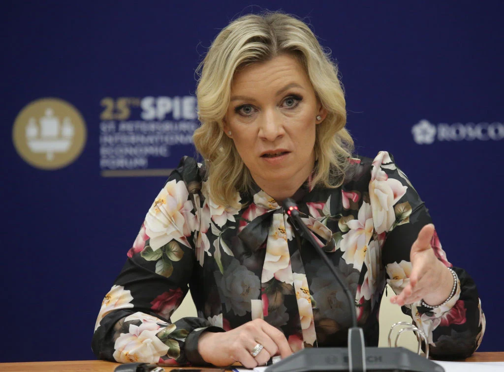 Marija Zacharowa, rzeczniczka MSZ Rosji Kobieta w blond włosach, ubrana w kwiecistą bluzkę, siedzi przy stole i mówi do mikrofonu. W tle znajduje się niebieska ścianka z logotypami i napisem związanym z forum ekonomicznym.