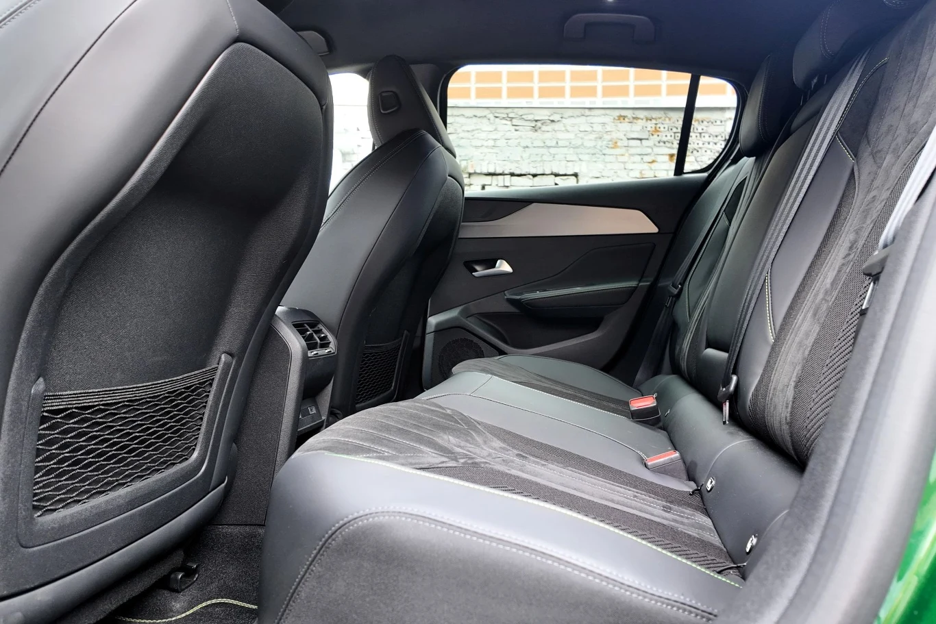 W drugim rzędzie Peugeota E-308 miejsca nie ma wyjątkowo dużo, ale na stosunkowo niewielkich odległościach jesteśmy w stanie podróżować dość wygodnie. Tylny rząd siedzeń w samochodzie, skórzana tapicerka, kieszenie na oparciach przednich foteli, widoczne detale wykończenia i fragment drzwi.