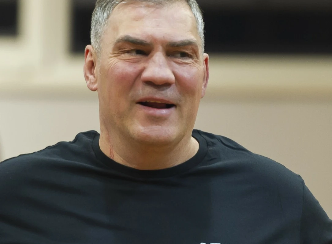 Dariusz Michalczewski w "Tańcu z gwiazdami"? Uśmiechnięty mężczyzna w średnim wieku z krótkimi siwymi włosami ubrany w czarną koszulkę, neutralne tło z rozmytym oknem.