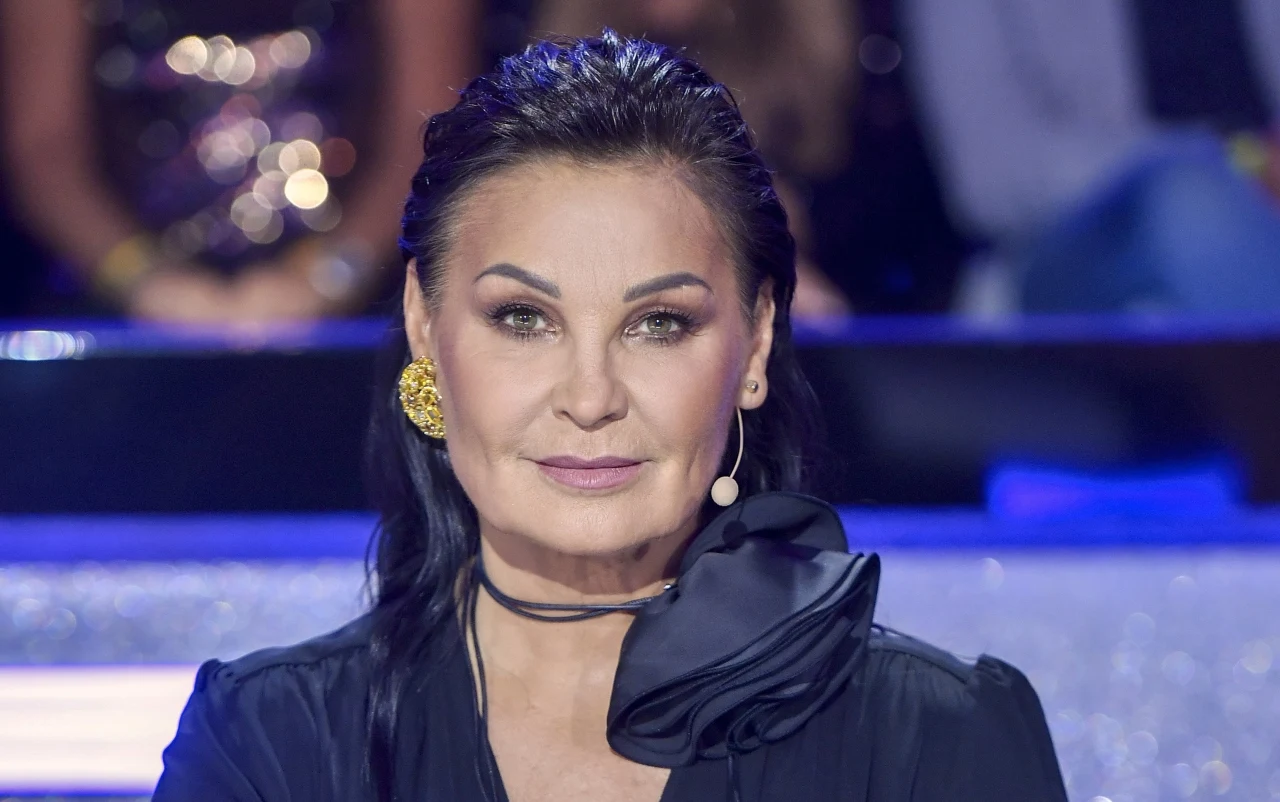 Iwona Pavlović w zaczesanych do tyłu włosach, w czarnej marynarce i z czarnym kwiatem na szyi