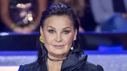 Iwona Pavlović w zaczesanych do tyłu włosach, w czarnej marynarce i z czarnym kwiatem na szyi