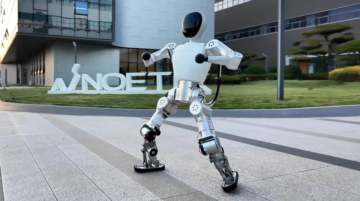 Robot humanoidalny w cenie iPhone'a. Kilka tys. złotych i jest twój. Ludzki robot w dynamicznej pozie na tle nowoczesnego budynku, w pobliżu logo firmy INOET, otoczenie urbanistyczne z dobrze utrzymaną zielenią.