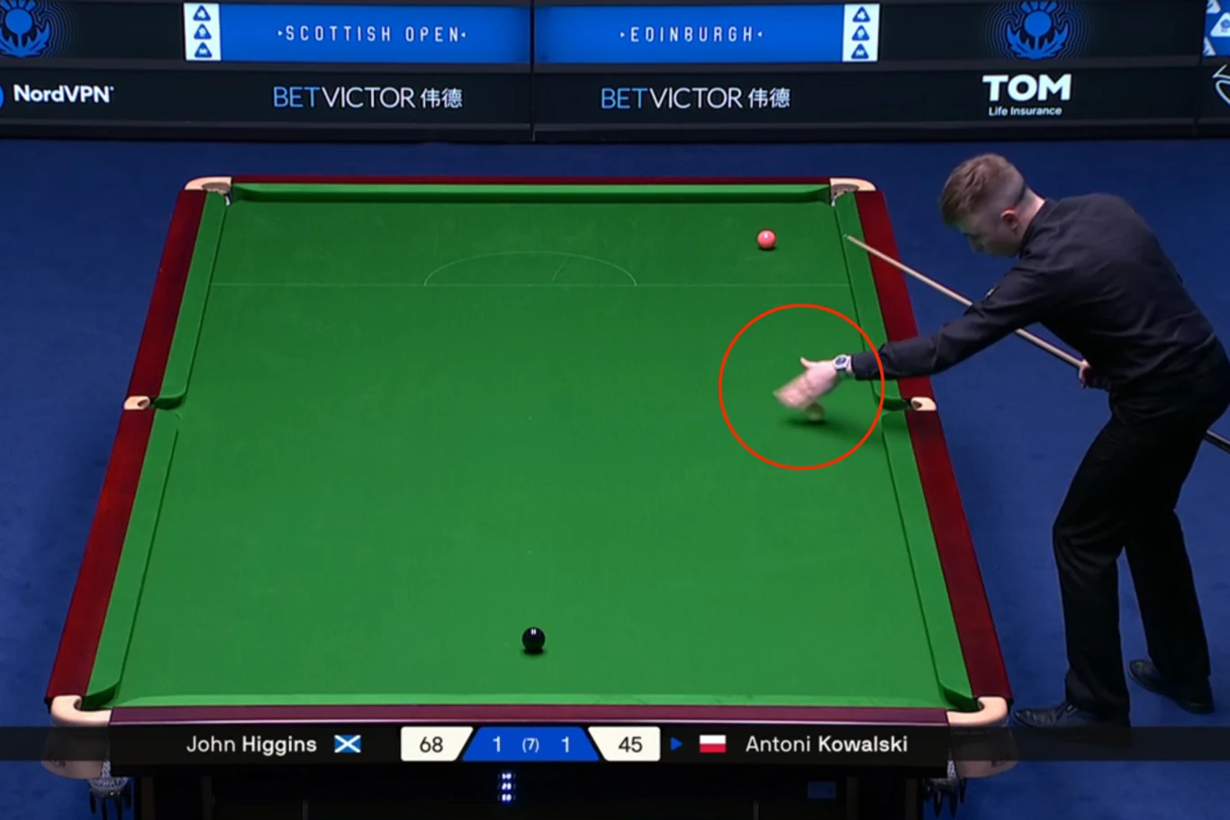 Zawodnik w trakcie rozgrywki snookera, przygotowujący się do uderzenia kija w bilę na profesjonalnym stole turniejowym. Tablica wyników pokazuje aktualny stan rywalizacji między Johnem Higginsem a Antonim Kowalskim.