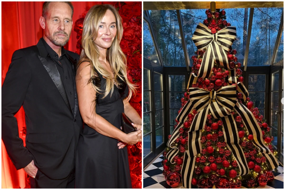 Para ubrana elegancko w ciemnych strojach stoi na tle czerwonych dekoracji, obok bogato ozdobiona choinka z wielkimi czarno-białymi kokardami oraz czerwonymi bombkami w przeszklonym pomieszczeniu.