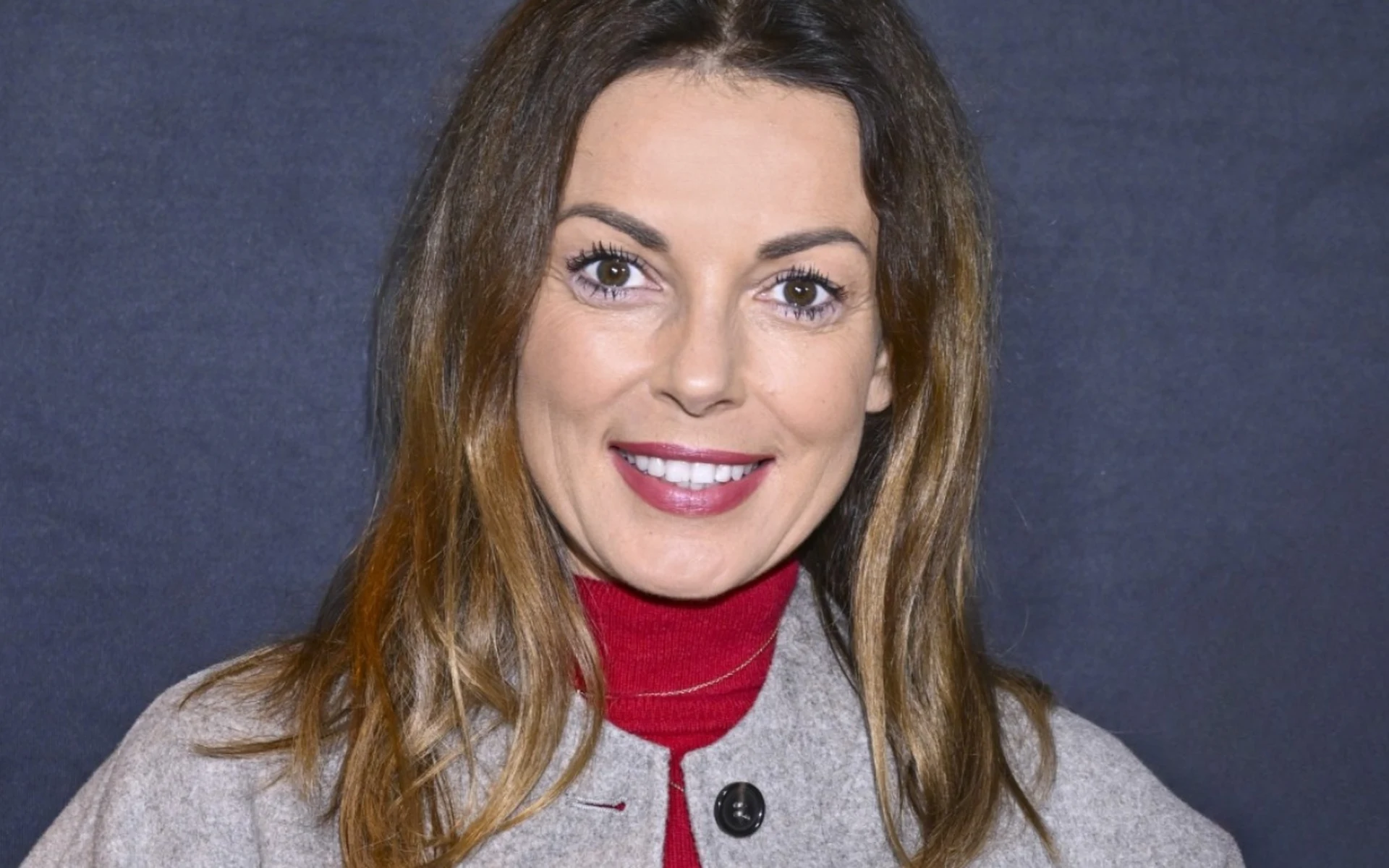 Katarzyna Glinka w czerwonej sukience i szarej kurtce, w rozpuszczonych włosach i czerwonej szmince