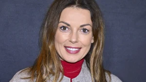 Katarzyna Glinka w czerwonej sukience i szarej kurtce, w rozpuszczonych włosach i czerwonej szmince